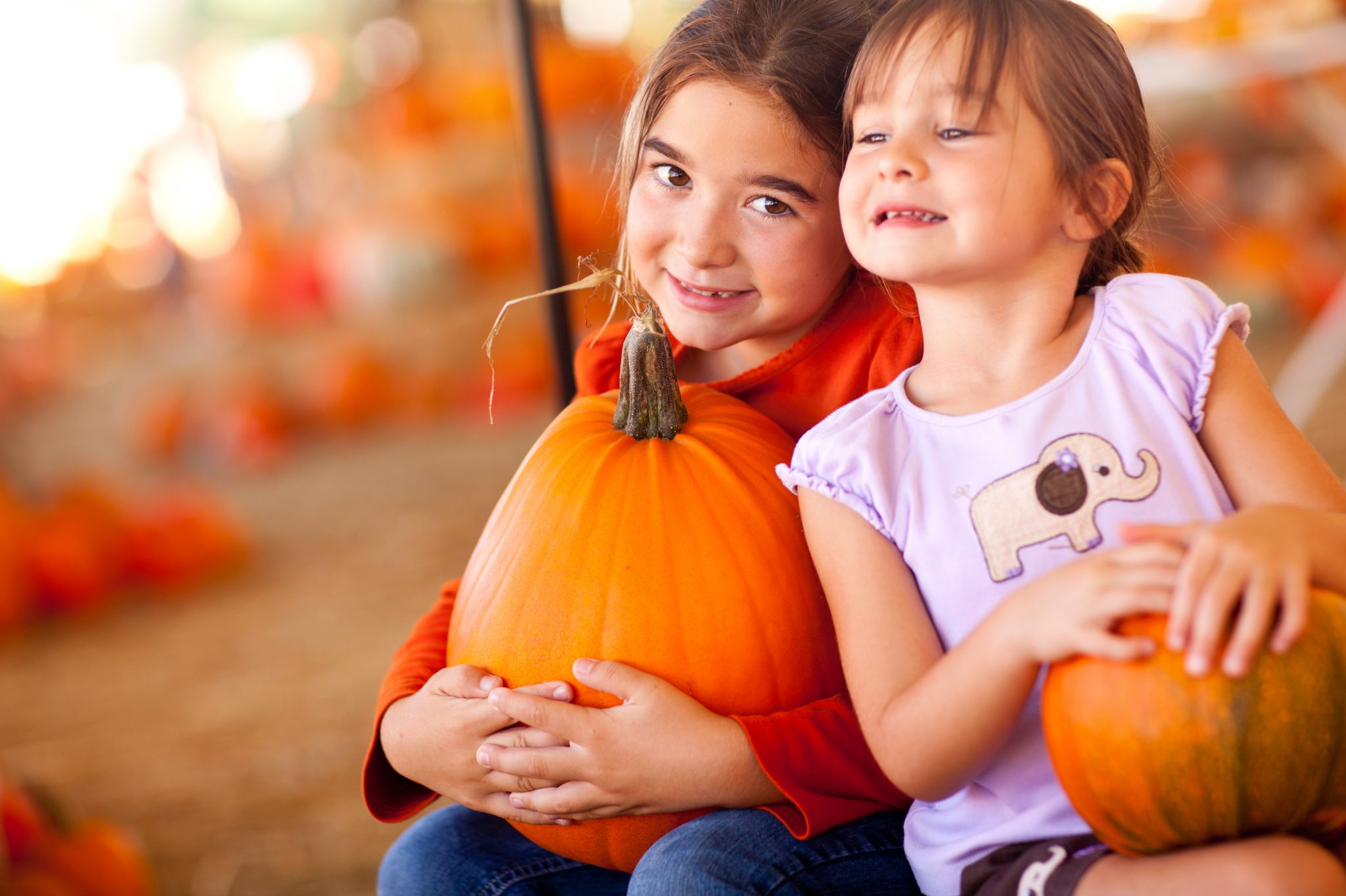 two girls smiling for the camera while holding pumpkins